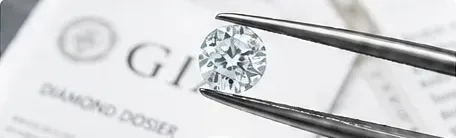 A diamond held in tweezers over a diamond report